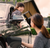 A child leans out of a car window, smiling at their parent who is plugging in a home EV charger.