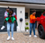 Outside a modern home, a parent plugs in an EV while their child gives the other child a piggyback ride.