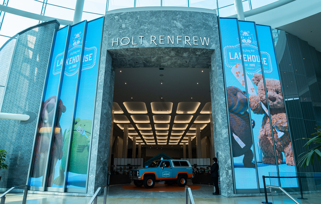 Entrée du grand magasin Holt Renfrew décorée aux couleurs de Jellycat Lakehouse, avec de grandes bannières bleues et un véhicule exposé à l’entrée.