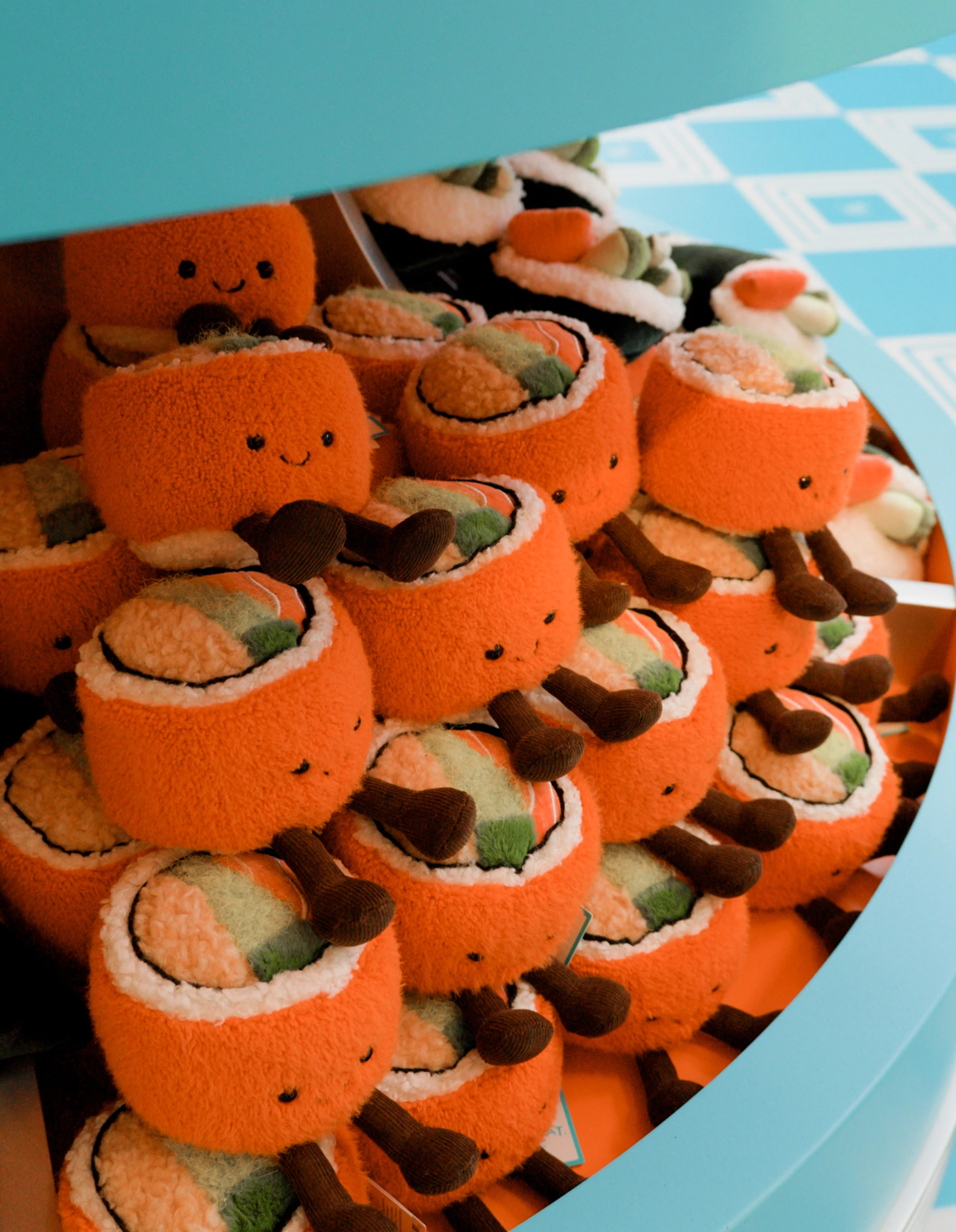 Assortiment Amuseables Codhi Californian Roll, empilées sur une étagère circulaire bleu turquoise dans l’espace Jellycat Cinema de Nordstrom The Grove.