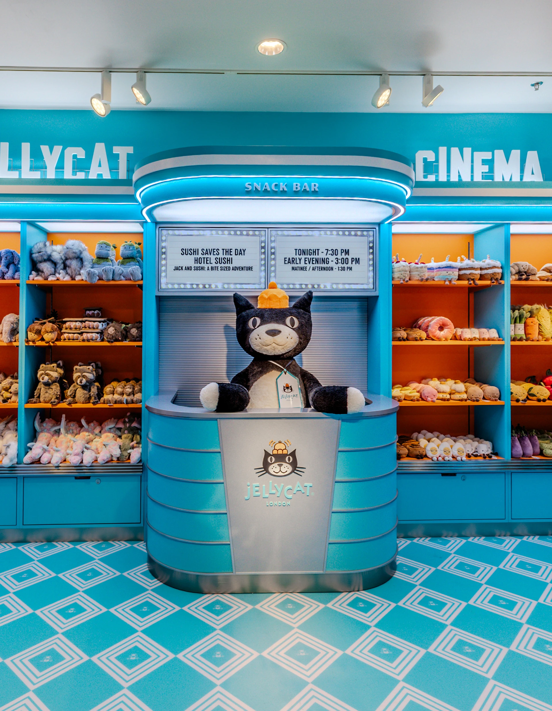 Comptoir inspiré d’un snack-bar de cinéma avec une grande peluche de Jellycat Jack en vedette, entourée d’étagères remplies de peluches colorées dans le décor rétro du Jellycat Cinema à Nordstrom The Grove.