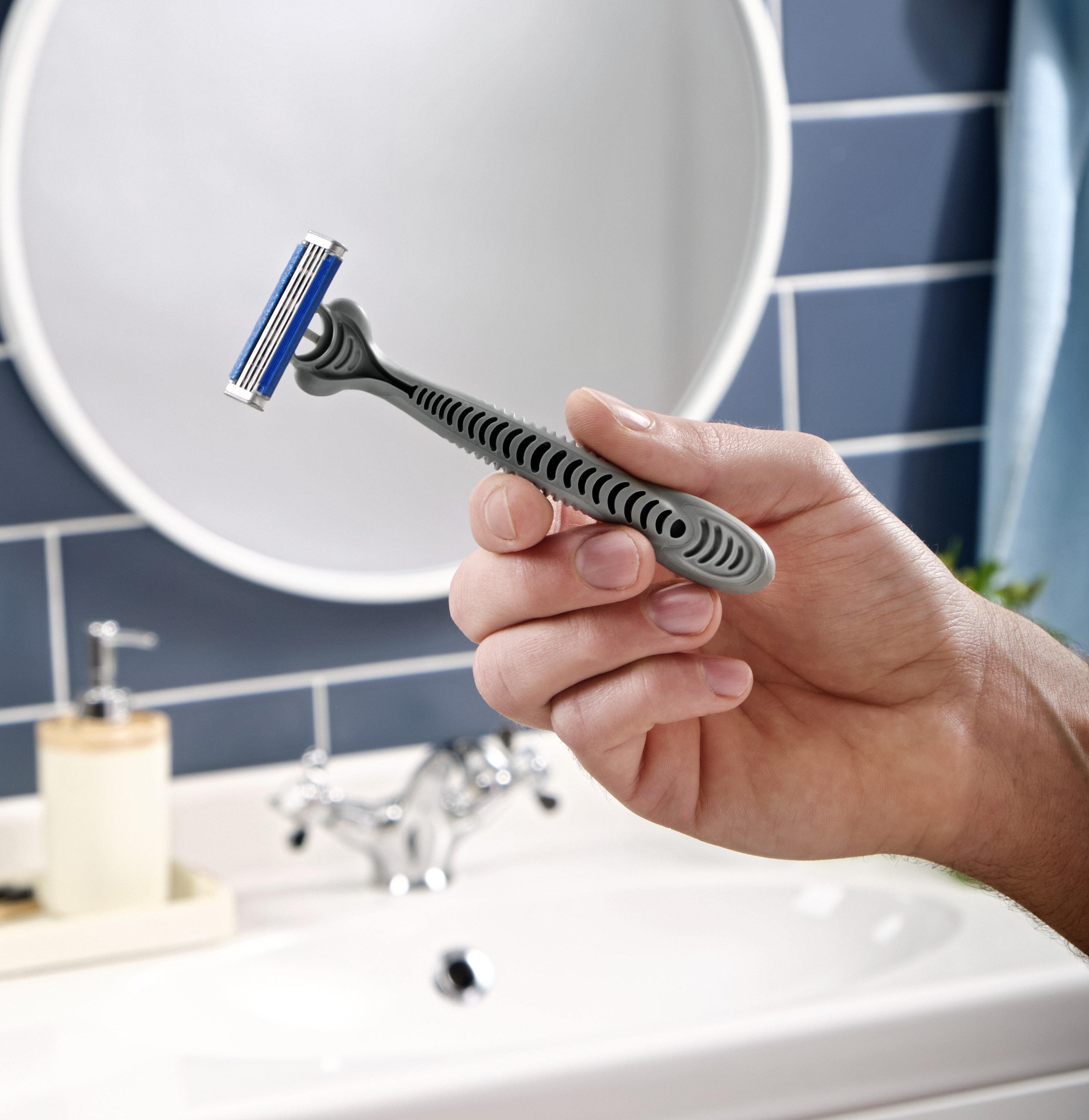 close-up of a hand holding a gray razor in front of a bathroom sink