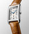 Longines DolceVita watch, rectangular stainless steel case with silver dial, blue hands, date display, and brown leather strap.