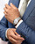 Longines The Longines Master Collection watch, men's wristwatch with silver and gold-tone stainless steel bracelet and white dial, worn on a man's wrist with a blue suit and beige tie.