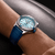 BREITLING Super Chronomat 38, luxury wristwatch with a light blue dial, diamond-studded bezel, and blue leather strap on a person's wrist.