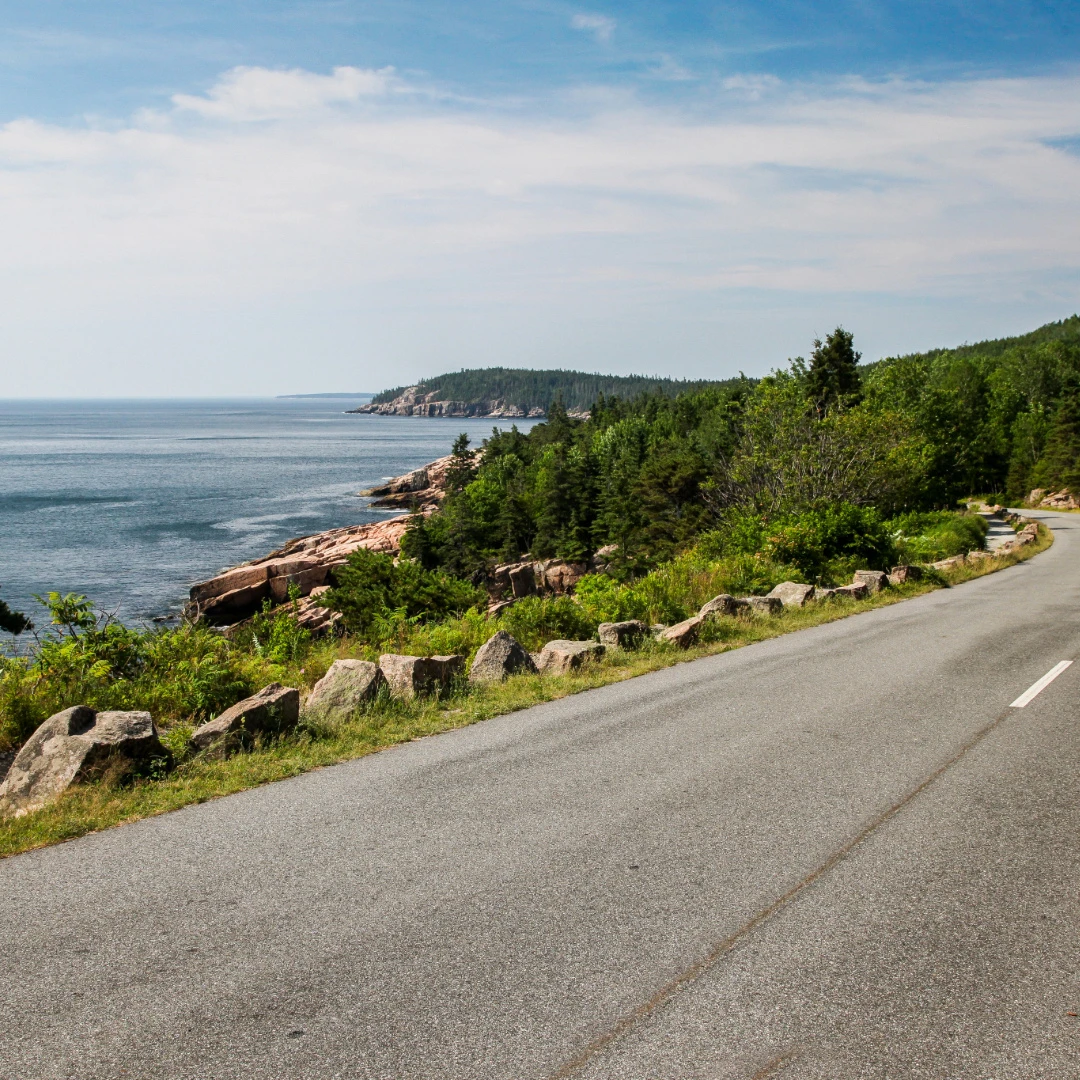 Coastal road winds past rocky shoreline and evergreen forests near Maine coastal towns.