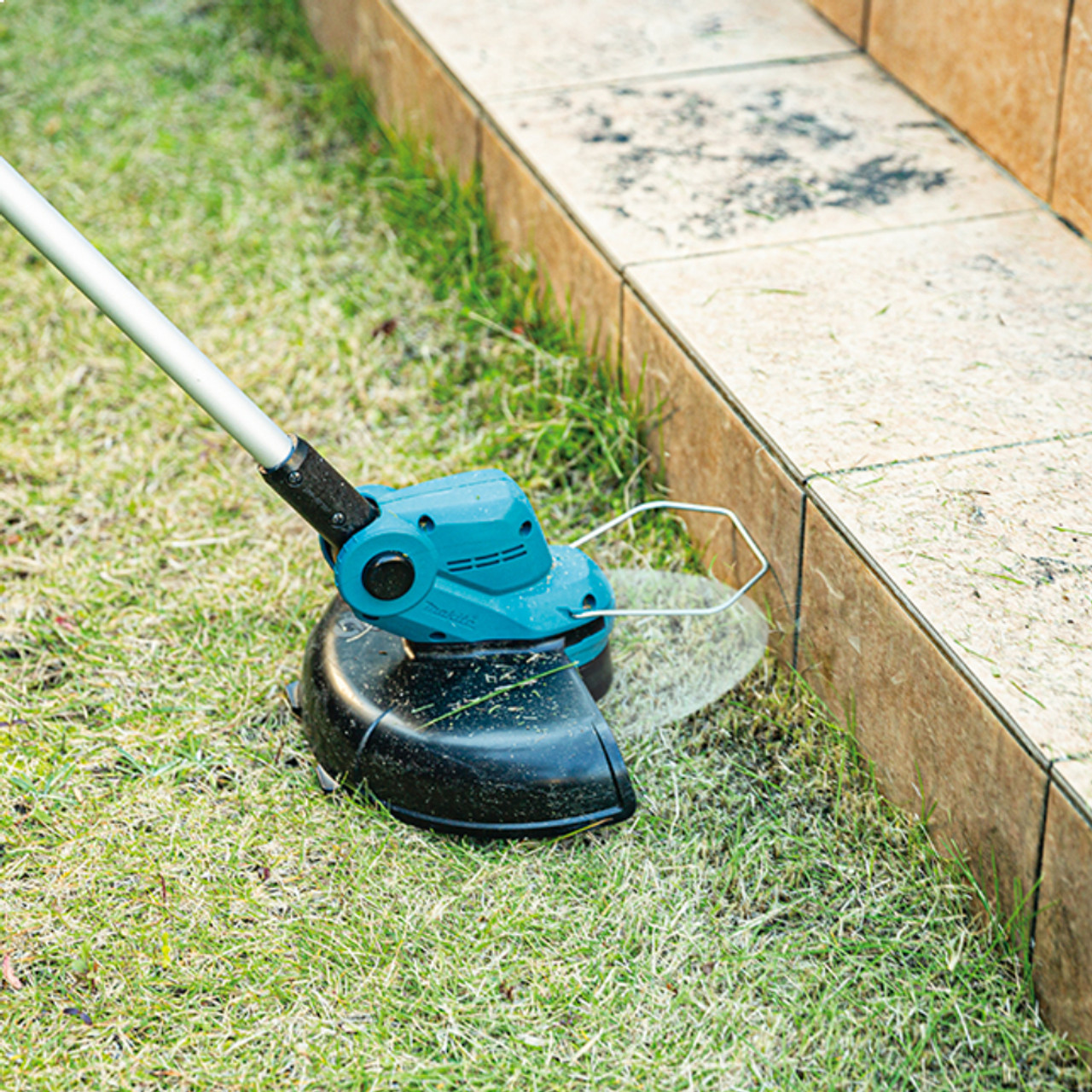 Makita DUR193Z 18V LXT Cordless 10-1/4 inch Line Trimmer (Tool Only) showing in use cutting grass allow wooden boarder Makita DUR193Z 18V LXT Cordless 10-1/4 inch Line Trimmer (Tool Only) showing in use cutting grass allow wooden boarder