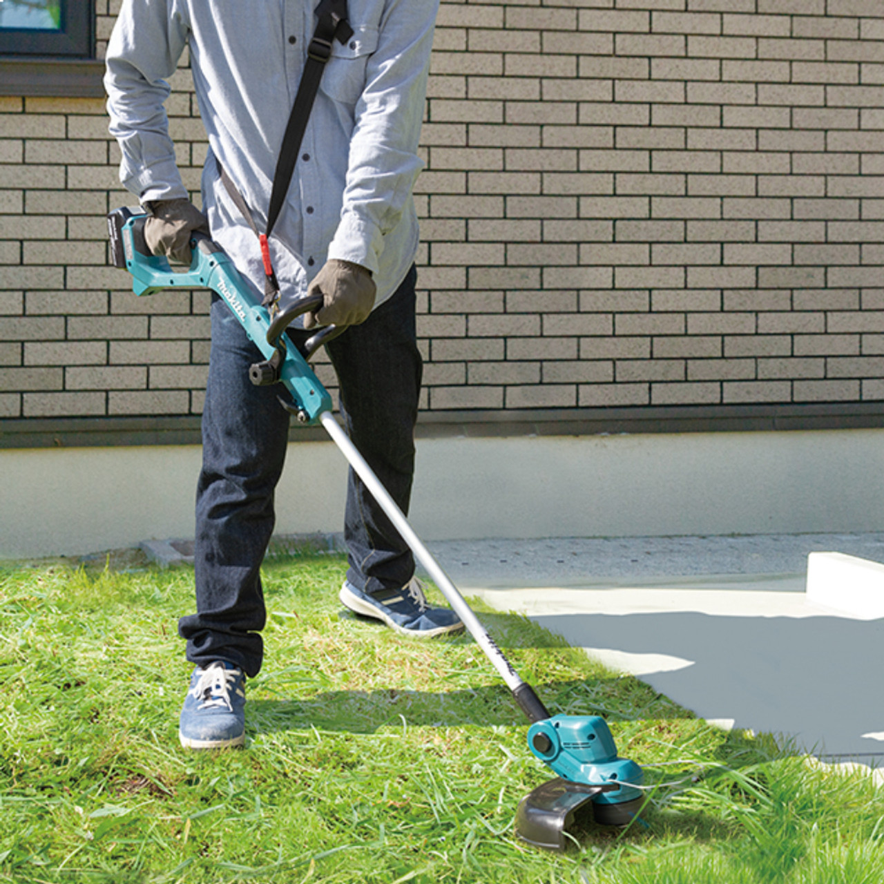 Makita DUR193Z 18V LXT Cordless 10-1/4 inch Line Trimmer (Tool Only) showing in use cutting grass along the side of a walk way Makita DUR193Z 18V LXT Cordless 10-1/4 inch Line Trimmer (Tool Only) showing in use cutting grass along the side of a walk way