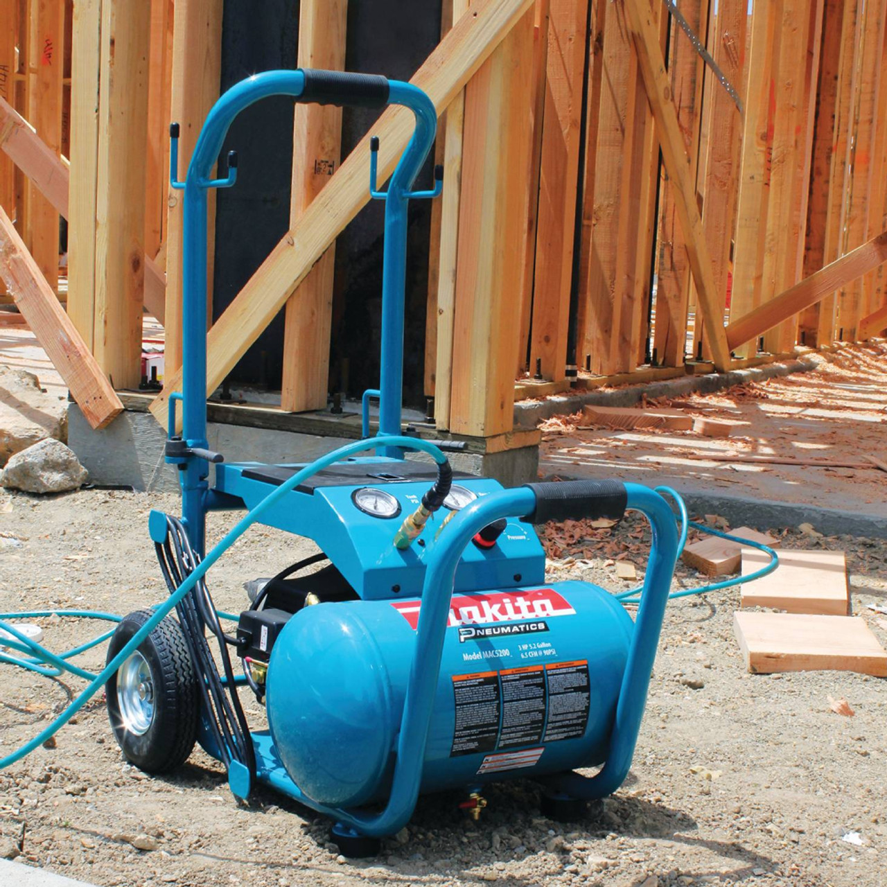 Makita MAC5200 13.8 Amp 3 HP Big Bore 5.2 Gallon Air Compressor showing compressor seating on a jobsite with air line plugged in Makita MAC5200 13.8 Amp 3 HP Big Bore 5.2 Gallon Air Compressor showing compressor seating on a jobsite with air line plugged in