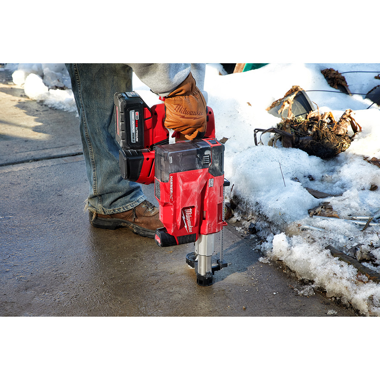 Milwaukee 2509-22 M12 HAMMERVAC Universal Dust Extractor Kit showing in use drilling into a concrete sidewalk (Hammer Drill sold separately)
