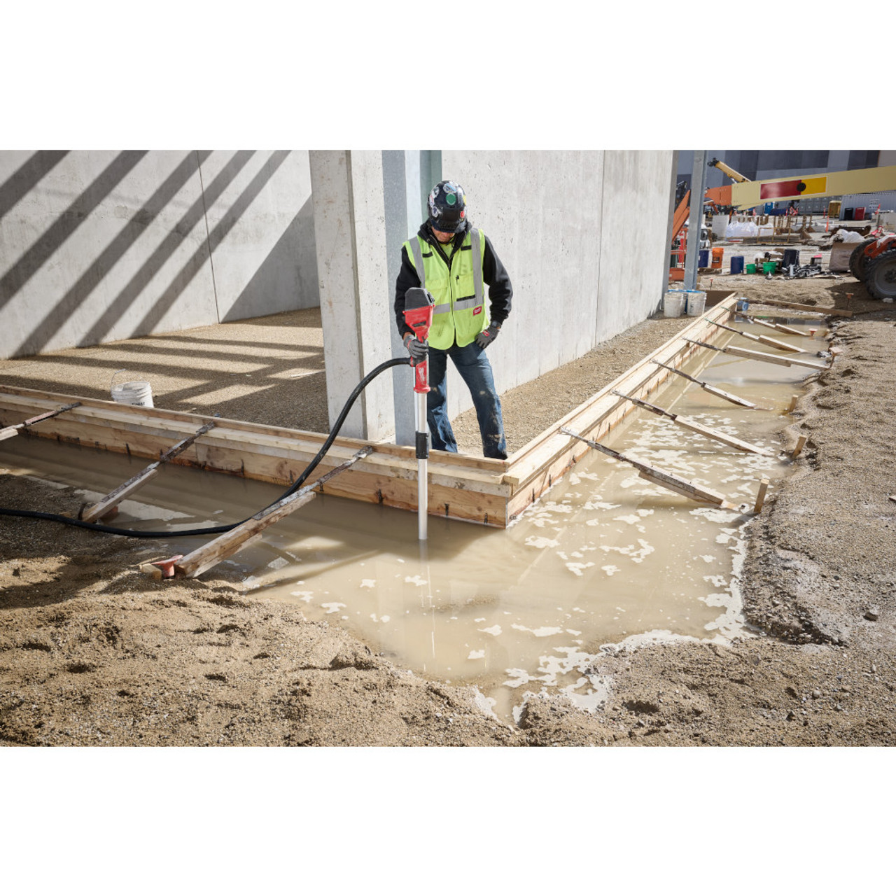 Milwaukee 2940-20 18V Brushless Stick Transfer Pump (Tool Only) showing in use removing water from a puddle next to a concrete forming