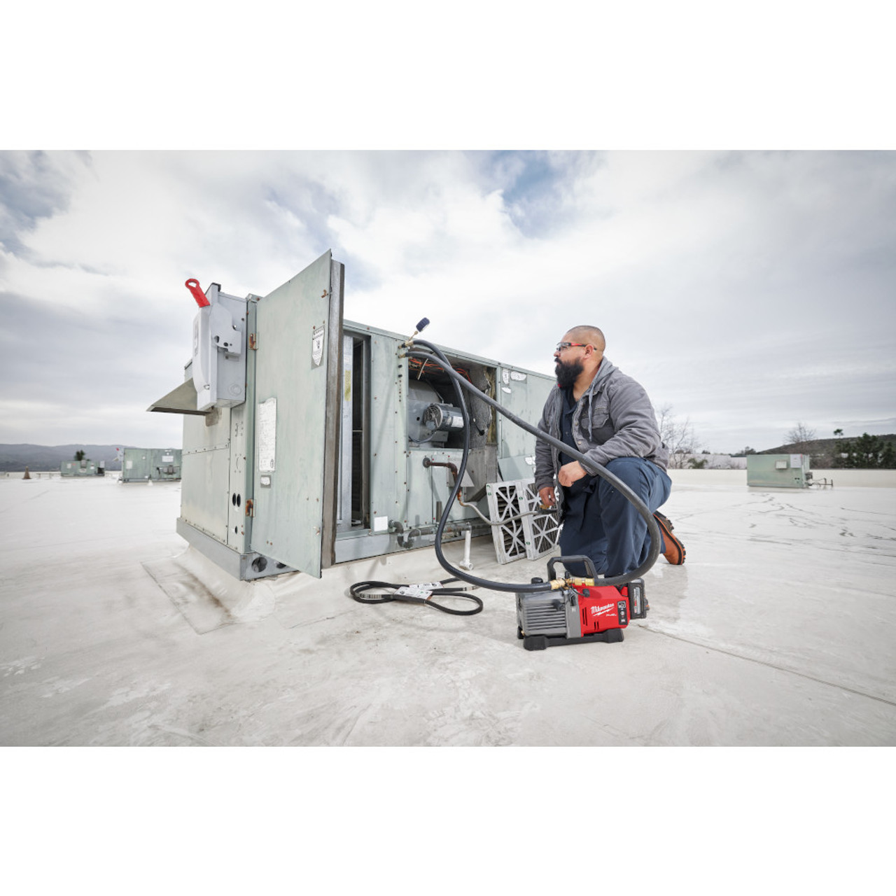 Milwaukee 2941-21 M18 FUEL 5 CFM Vacuum Pump Kit showing in use cleaning out a cavity inside a commercial air conditions
