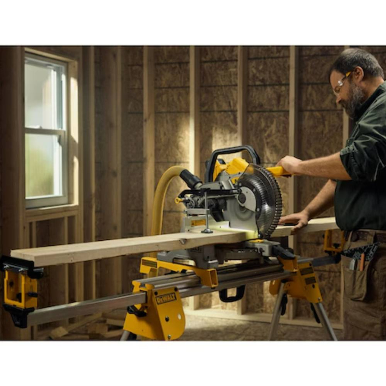 DeWalt DCS714B 20V MAX XR Cordless 10in Double Bevel Fixed Mitre Saw (Tool Only) showing in use cutting wood stud with saw mounted on stand with vacuum attached (Battery, stand, and vacuum sold separately)