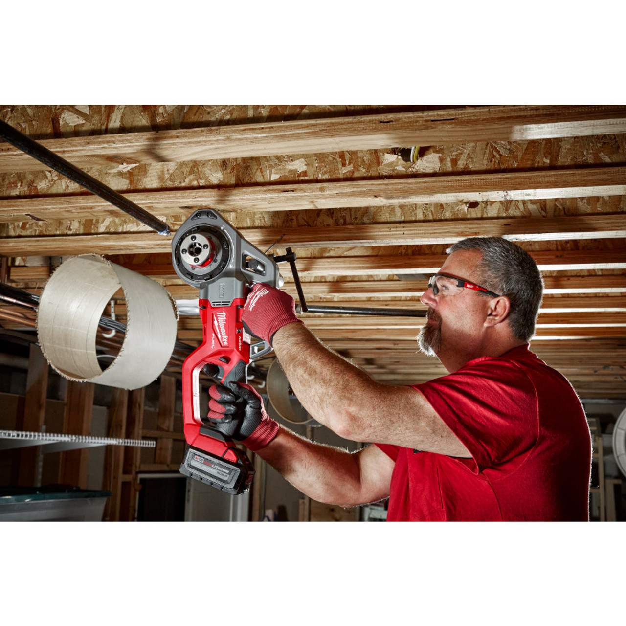 Milwaukee 2870-22 M18 FUEL Cordless Compact Pipe Threader with 1/2 inch - 1-1/4 inch Die Heads Kit showing in use threading pipe while mounted in ceiling during installation Milwaukee 2870-22 M18 FUEL Cordless Compact Pipe Threader with 1/2 inch - 1-1/4 inch Die Heads Kit showing in use threading pipe while mounted in ceiling during installation