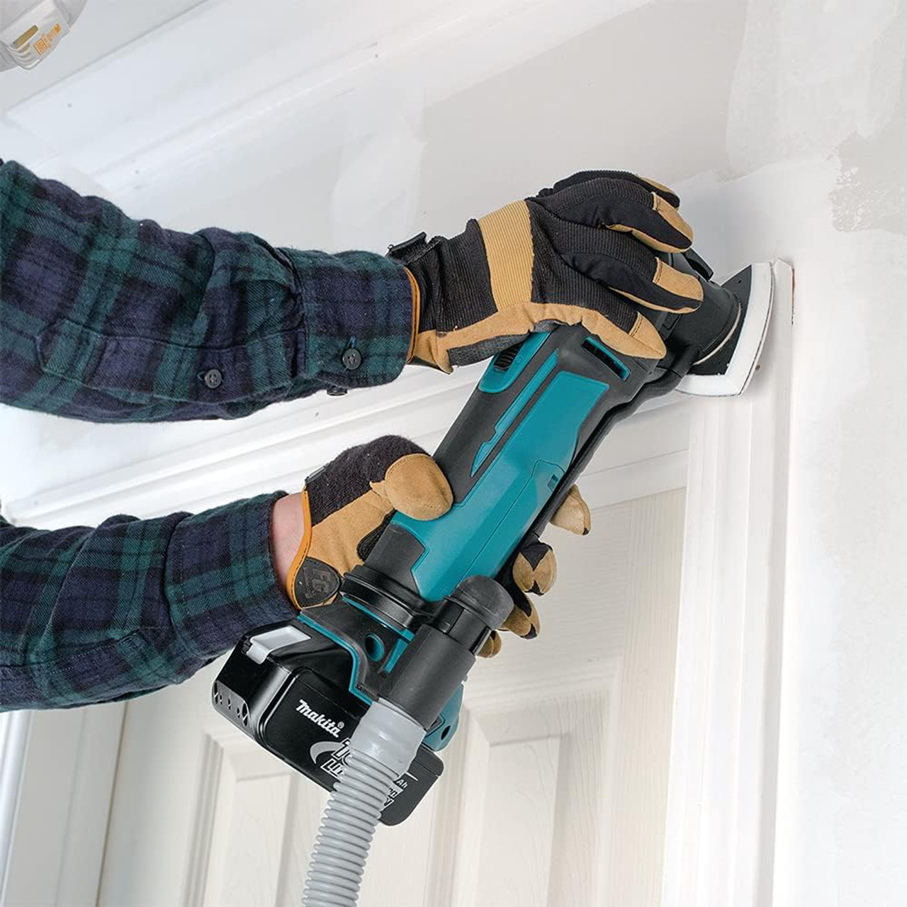 Makita DTM51Z 18V LXT Cordless Multi-Tool (Tool Only) showing in use sanding door casing/molding with vacuum attachment (Vacuum attachment sold separately)