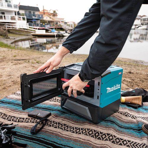 Makita MW001GZ 40V max XGT Microwave Oven (Tool Only) showing in use putting a container in the microwave oven for a hot lunch (Battery sold separately)