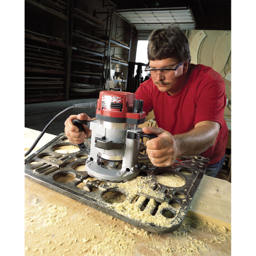 Milwaukee 5625-20 22 Amp 3-1/2 Max HP Fixed-Base Production Router showing in use cutting into a wood plank with a template jig (Jig sold separately)