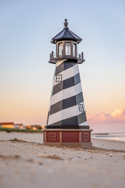 Amish Made Wood-Poly Hybrid Lighthouse - Cape Hatteras - Shown As: 5 Foot, Standard Electric Lighting, Poly Roof/Top Color: Black, Wood Tower Primary Color: Black, Wood Tower Accent Color: White, Poly Base Primary Color: Cherrywood, Poly Base Trim Color: Weatherwood, pictured on beach at sunset.