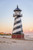 Amish Made Wood-Poly Hybrid Lighthouse - Cape Hatteras - Shown As: 5 Foot, Standard Electric Lighting, Poly Roof/Top Color: Black, Wood Tower Primary Color: Black, Wood Tower Accent Color: White, Poly Base Primary Color: Cherrywood, Poly Base Trim Color: Weatherwood, pictured on beach at sunset.