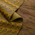 Mustard yellow leather with black leaf pattern, showcasing texture on rustic wood surface