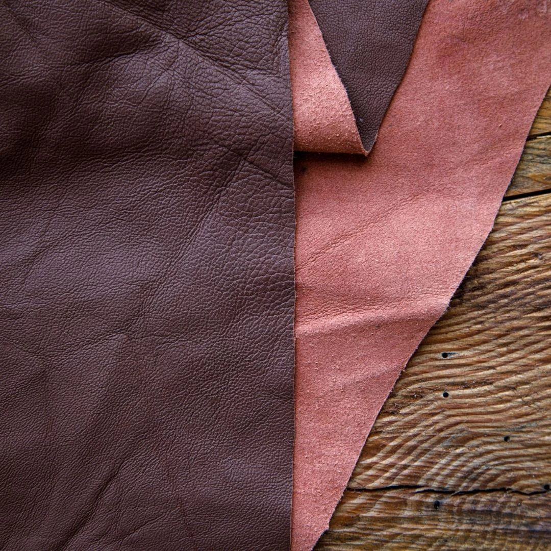 Rich brown and dusty rose leather hides on rustic wood, showcasing natural grain for crafting and upholstery.