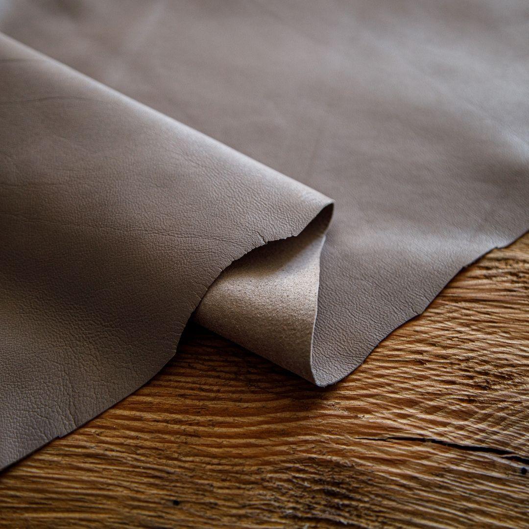 Premium tan cowhide leather hide with natural grain, displayed on rustic wood surface for crafting