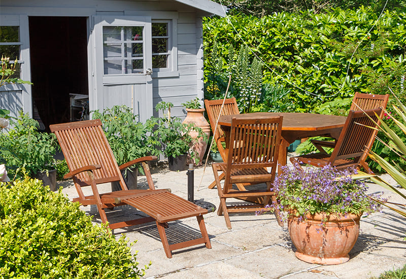 Een tuin in de zon, met houten gebeitste tuinset, en een houten gebeitste tuinhuis.