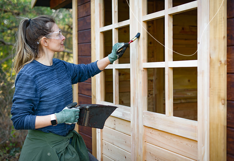 Een vrouw die haar tuinhuis aan het schilderen is.