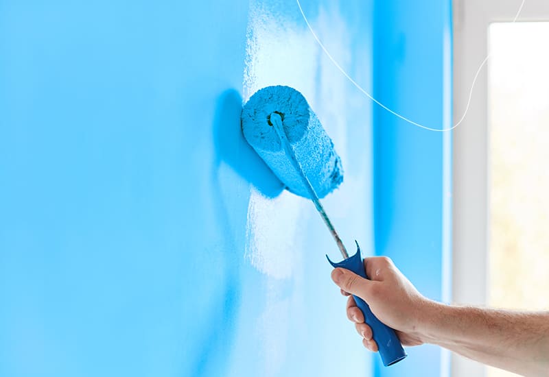 Iemand brengt blauwe watergedragen muurverf aan op de binnenmuur.