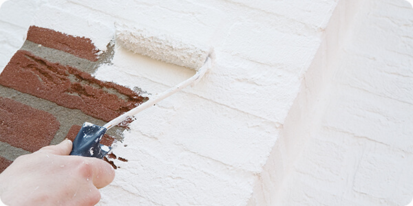 Witte buitenmuurverf wordt met een kleine verfroller aangebracht op een bakstenen buitenmuur.