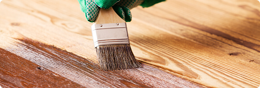 Dekkende bruine binnenbeits wordt met een platte kwast aangebracht op een houten vloer