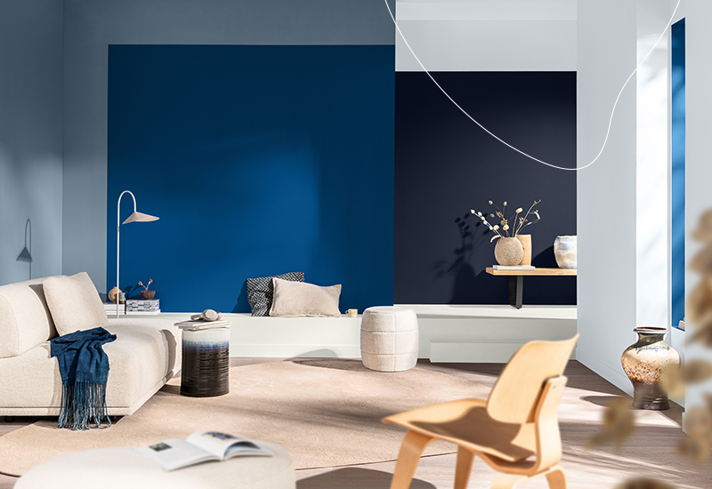 Woonkamer met beige bank en houten stoel, met grote kleurvlakken in kobaltblauw en diep marineblauw op de muren, in zacht daglicht.