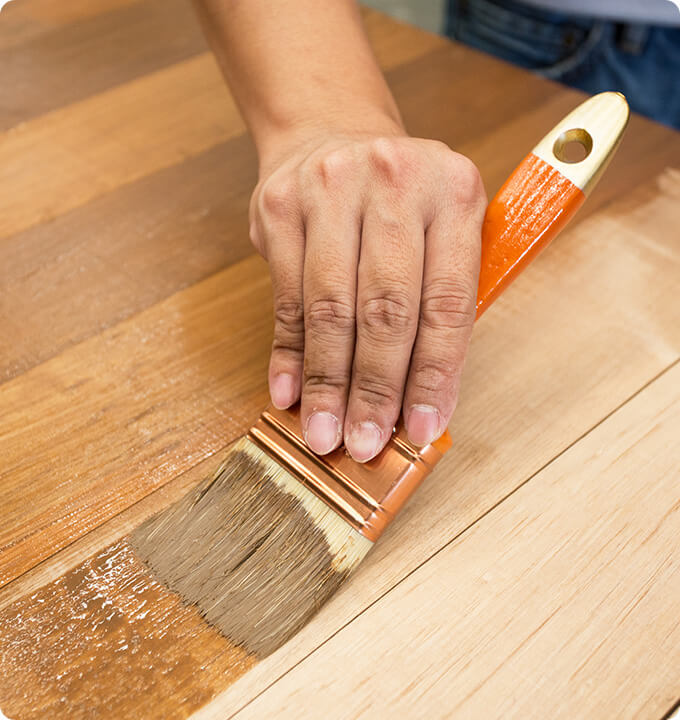 Kleurbeits met een eiken kleur wordt met een platte kwast aangebracht op een tafel