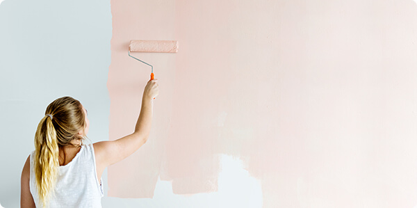 Een vrouw die met licht roze krijtverf de muur behandeld en een poedermat effect geeft.