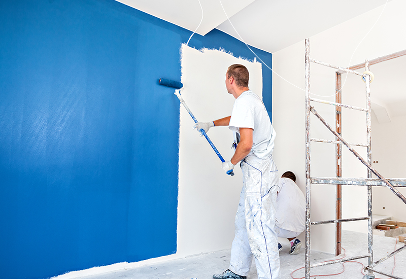 De schilder verft met blauwe muurverf de hele muur.