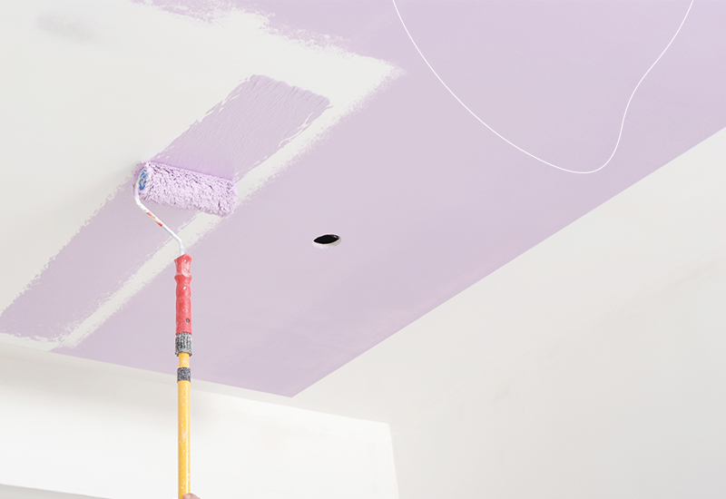 Een plafond wordt geverfd in een lichtpaarse kleur doormiddel van een roller.