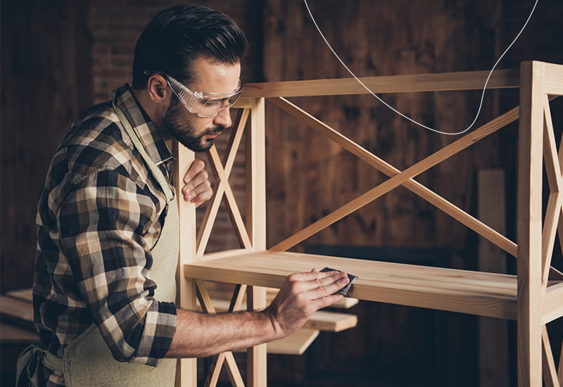 Een man schuurt een houten tuinbank met schuurpapier.
