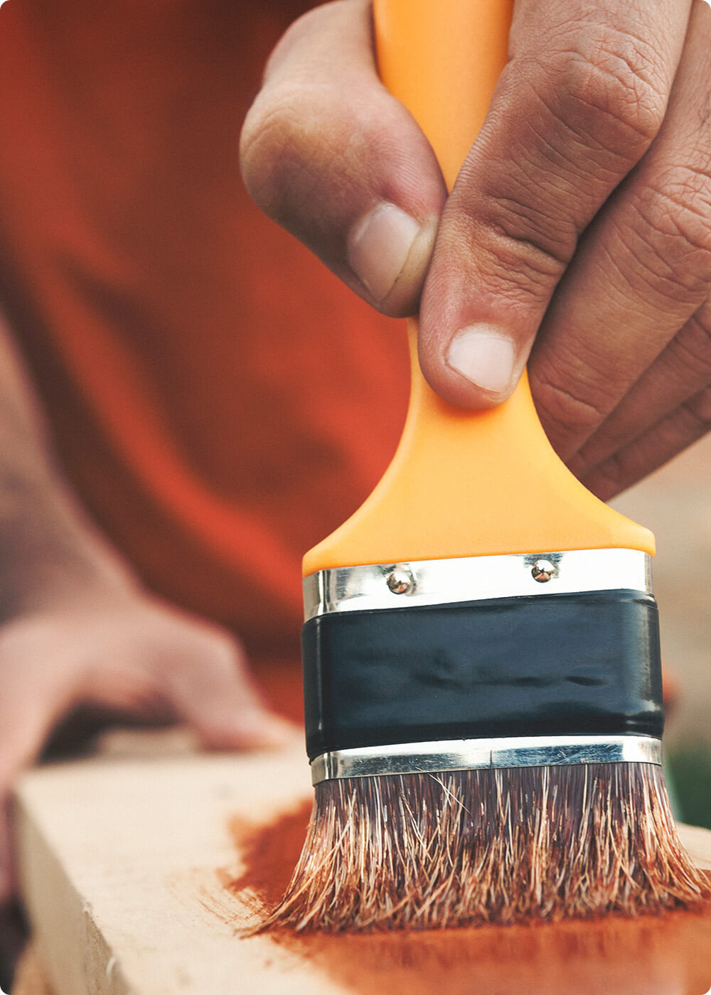 Close-up van roodbruine steigerhoutbeits die met een kwast wordt aangebracht op steigerhout.