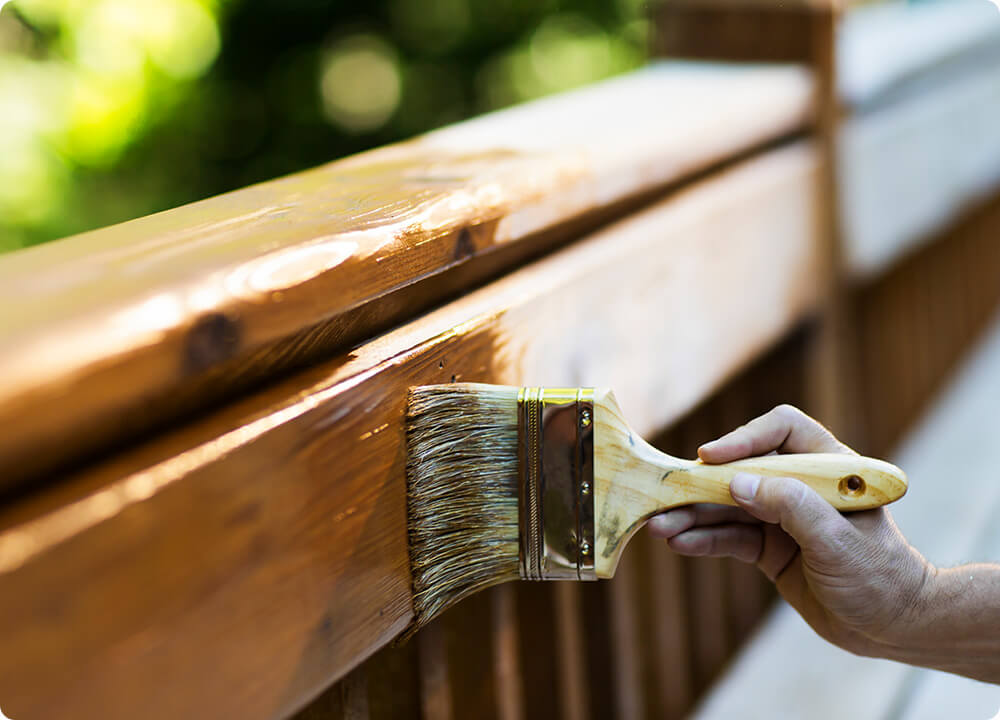 Transparante beits wordt met een platte kwast aangebracht op een houten oppervlak