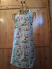 Handmade light green apron featuring a whimsical full‑meadow gnome print with no pocket and coordinating head loop and waist ties