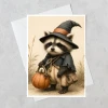 greeting card featuring a whimsical woodland raccoon holding a pumpkin displayed with a white envelope