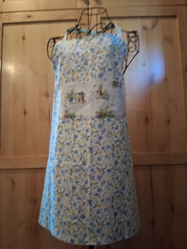 Handmade white floral apron showcasing a Beatrix Potter Peter Rabbit pocket with coordinating straps and delicate meadow blossoms