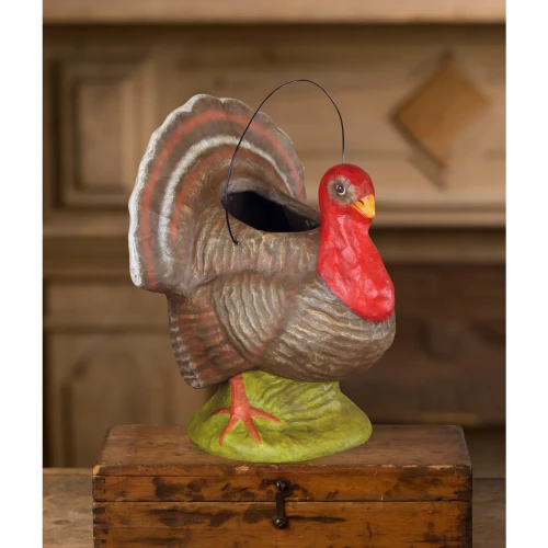 Hand‑painted vintage‑style paper mâché turkey with red head, brown feathers, grassy base, and wire handle.