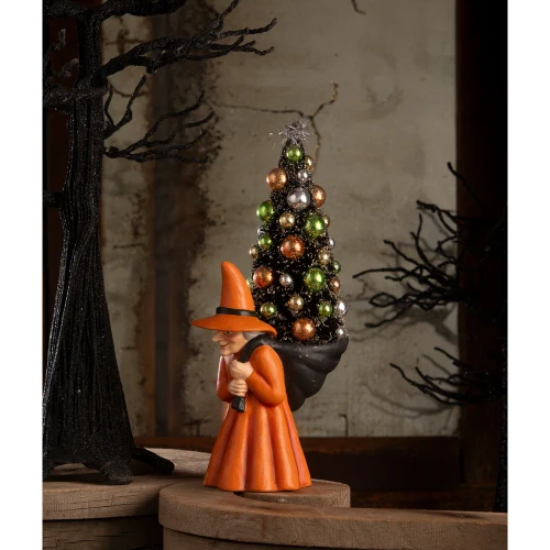 Vintage hand‑painted witch figurine in orange robe holding a decorated bottle brush tree.