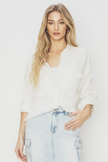 A person stands against a bright background, modeling the Everyday Joy Shirt, an oversized, soft tencel fabric shirt with roll tab sleeves. The shirt has a full button front closure and is paired with light denim jeans for a comfortable, casual look.