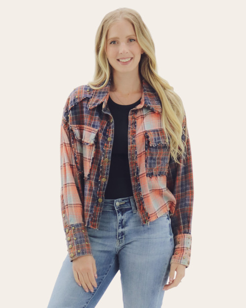Front view of a woman wearing a cropped plaid shacket in navy, rust, and sea green tones, styled with a black top and light-wash jeans.