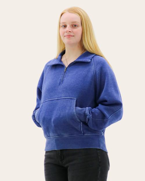 Front view of a woman in a blue quarter-zip sweatshirt with a relaxed fit and kangaroo pocket.