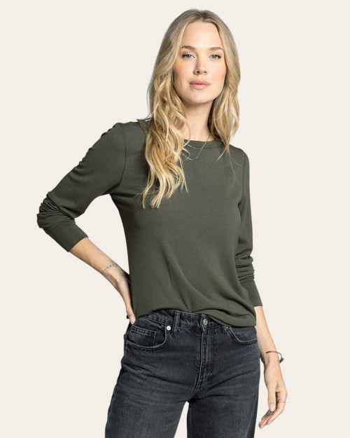 Woman wearing a eucalyptus green long sleeve top tucked slightly into black jeans, posing front-facing.