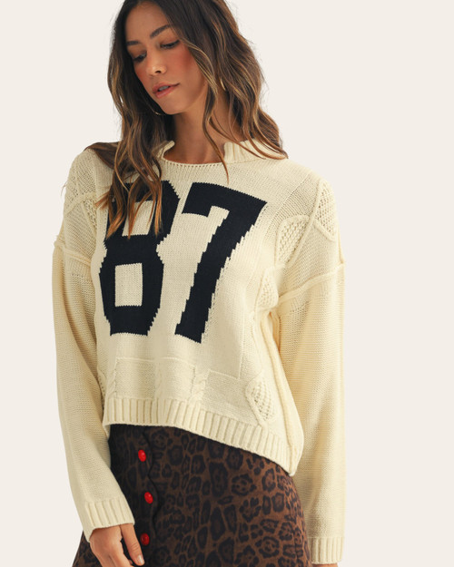 Front view of the Vintage 87 Sweater in cream featuring bold black numbering and a notched neckline, available at Trendy Threads.