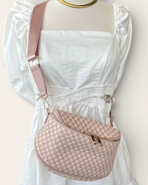 Front view of the Light Pink Checkered Saddle Crossbody Bag worn over a white dress, featuring a vegan leather woven design and wide strap.